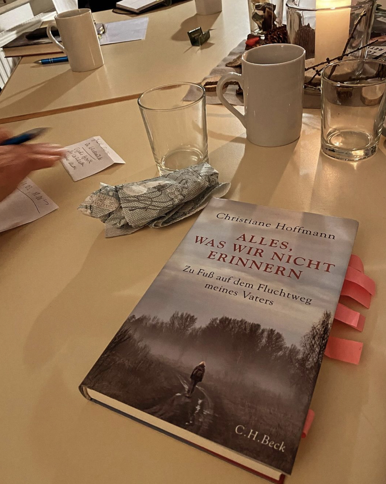 Ein Buch auf einem Tisch mit einer Person, die in einem dunkeln Wald läuft. Christiane Hoffmann, Alles was wir nicht erinnern.